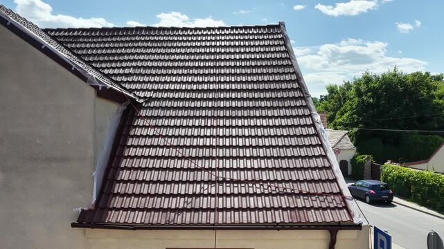 Roof renovation process with spray painting of roof tiles, including priming and applying second coat of paint on a residential roof, showing professional exterior maintenance and refurbishment work.