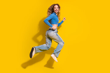 Cheerful young woman in casual outfit jumping joyfully against a yellow background, expressing...
