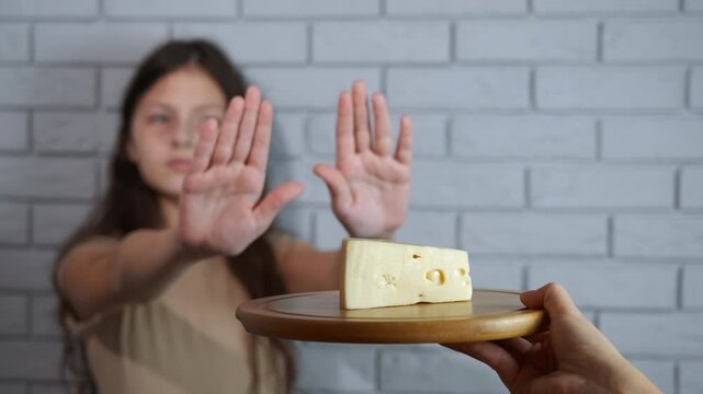 Lactose intolerance. Unhappy teenage girl with lactose intolerance making a stop gesture with her hands, refusing a piece of cheese because of her dietary restrictions and food allergy