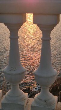 Sunset sea balustrade overlooking a peaceful golden sunset over the calm ocean through classic white stone architectural balusters