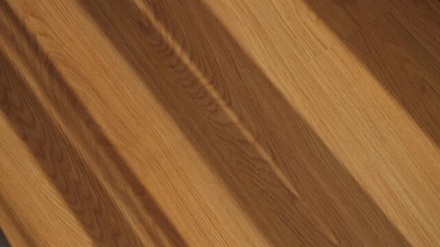 Wooden planks with natural grain patterns and warm tones. Diagonal lines created by window curtain moving and waving in the wind. Sunlight shining in. Textured surface shows subtle wood grain details