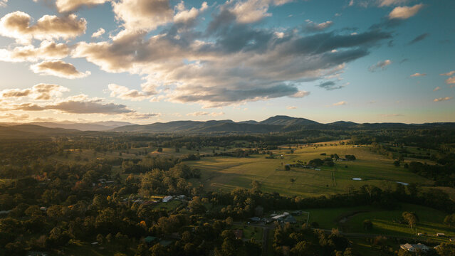 Aerial view of rolling hills, lush green pastures, scattered trees, and a dramatic sunset sky in Beechwood, New South Wales, Australia.