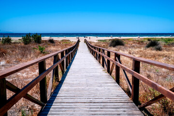 Naklejka premium Wooden entrance to Los Lances Beach with people relaxing, Tarifa. Postcard from Costa de la Luz, Spain.