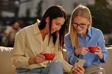 Fototapeta na wymiar Women friends laughing looking at smartphone together