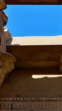 Kom Ombo temple columns with composite capitals and hieroglyphic carvings viewed from below against blue sky in Egypt, upward perspective of ancient sandstone architecture