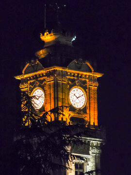 Close-up shot of Ottoman architecture clock tower with glowing dials against dark night sky.
