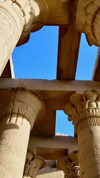 Kom Ombo temple columns with composite capitals and hieroglyphic carvings viewed from below against blue sky in Egypt, upward perspective of ancient sandstone architecture