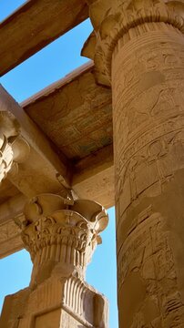 Kom Ombo temple columns with composite capitals and hieroglyphic carvings viewed from below against blue sky in Egypt, upward perspective of ancient sandstone architecture