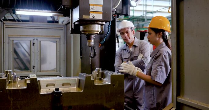 Asian woman technician checks component near CNC machine while Asian man engineer reviews result, supporting quality assurance, verification, and safe communication during precision metal production