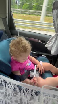 Little girl sitting in car seat holding white lace parasol. Toddler playing with umbrella during road trip. Playful child in vehicle, childhood travel journey.
