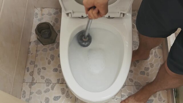 Man uses toilet brush to clean the white porcelain bowl in a bright bathroom, wearing casual attire