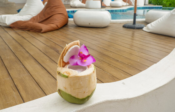 Tropical fresh coconut cocktail decorated with flowers and sandy beach by the sea,tropical resort villa,island summer travel,ocean backdrop,hotel for holiday vacation concept.
