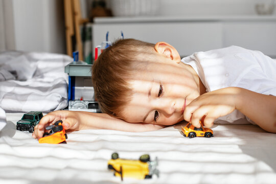 Little boy playing with toy cars on bed in sunny room, childhood and imagination concept