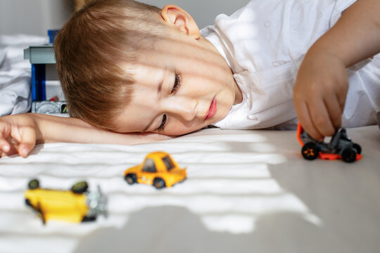Little boy playing with toy cars on bed in sunny room, childhood and imagination concept