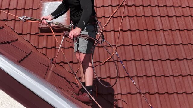 Roof renovation process with spray painting of roof tiles, including priming and applying second coat of paint on a residential roof, showing professional exterior maintenance and refurbishment work.