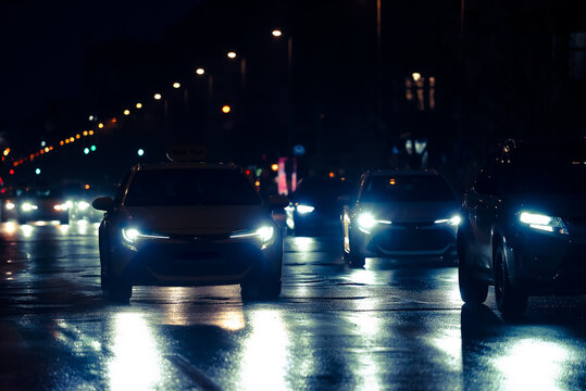 Night city traffic with cars driving on a wet asphalt road with bright headlights and reflections