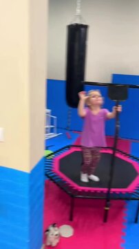 Little girl jumping on fitness trampoline in gym. Child exercising indoor on rebounder with boxing bag. Active kid having fun during sports activity training.