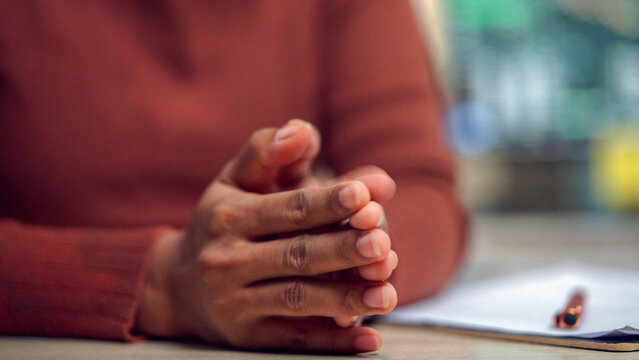 Hands clasped together show quiet focus or anticipation. Fingers interlaced, palms resting, suggest patience or thoughtfulness. Wearer wears a warm, earth-toned sweater