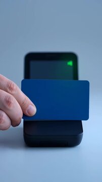 Hand holding blue contactless card near payment terminal.