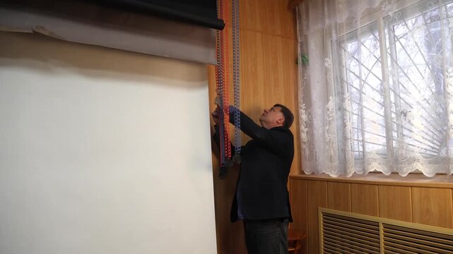 A male photographer inspects the chains of a lifting mechanism used to support a paper backdrop in a photography studio.