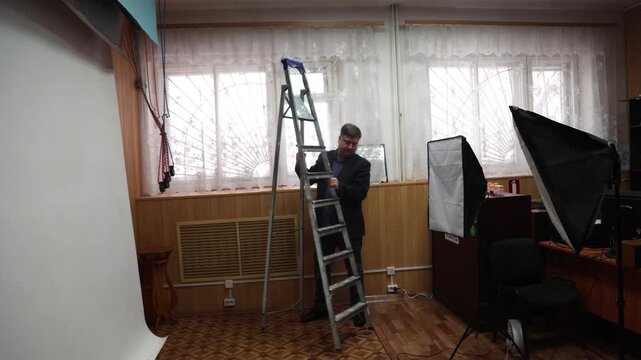 A worker sets up a tall stepladder in a professional photography studio for installation or maintenance of equipment.