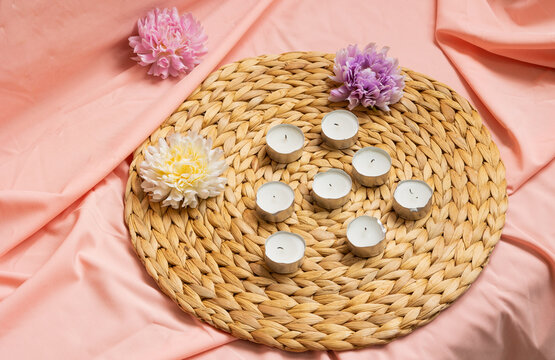 Top view of spa candles next to flowers on a pink tablecloth. Concept of relaxation, wellness, self care, harmony, beauty, and a relaxing atmosphere