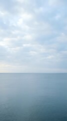Obraz premium Serene seascape with calm ocean waters and soft cloudy sky, suitable for backgrounds, travel websites, and peaceful nature compositions.