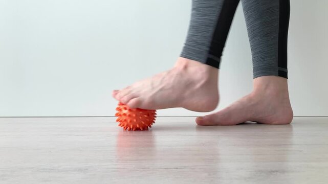 A woman relaxes her feet after a long walk, rolls a massage ball from the heel to the toe, restoring lightness, relieving fatigue and tension. Close-up