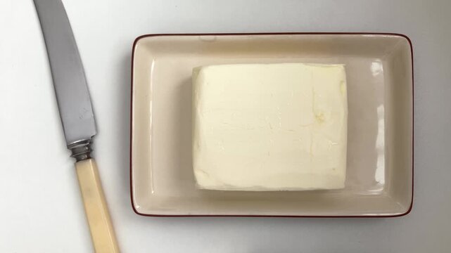 Top view of an oil pan on a white table. A woman's hand opens the lid, a block of butter. Convenient storage allows you to always have butter on hand for breakfast or a snack