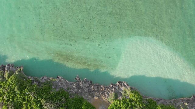 Top down aerial view of crystal clear emerald green ocean and rocky shoreline in Miyakojima, Okinawa