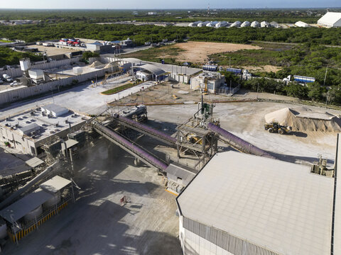 Aerial view of Cemento Jaguar cement plant featuring industrial conveyor belts, storage buildings, and heavy machinery in the facility grounds in Progreso, Yucatan, Mexico.