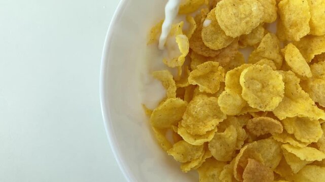 Milk is poured into a white bowl with cornflakes on a white background. Top view of a bowl of cereal. A quick breakfast for satiety, energy and vitamins, a popular choice for children and adults