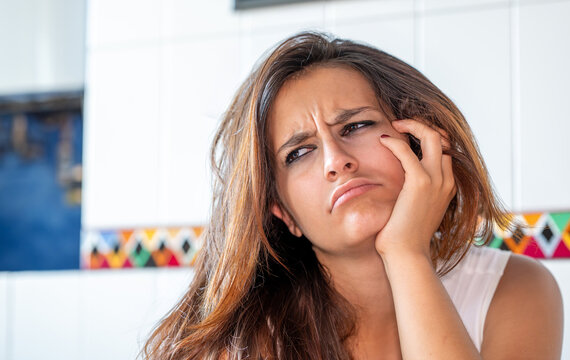 Young frustrated woman with messy hair supporting her head with a hand, feeling bored, tired, and unmotivated while looking away