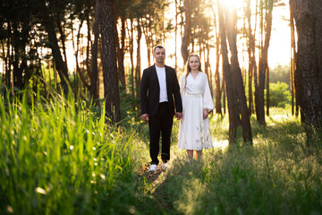 Fototapeta premium Couple holding hands in a sun-drenched forest during golden hour