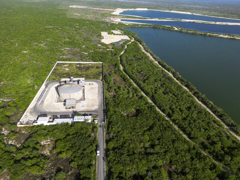 Aerial view of Aguadas de Flamboyanes with a circular storage tank in a fenced compound, surrounded by vegetation and water bodies in Campestre Flamboyanes, Yucatan, Mexico.