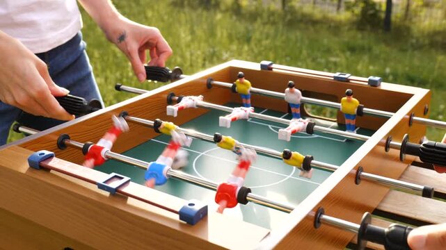 Two person playing table foosball with red and yellow plastic players in a garden, capturing everyday joy and simple outdoor fun.