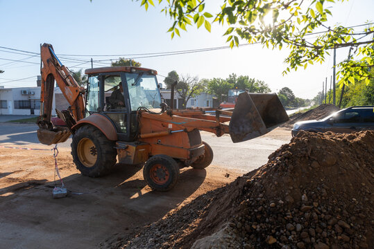 Orange Backhoe Loader Excavator Next to Dirt Pile on Urban Street Construction Site
