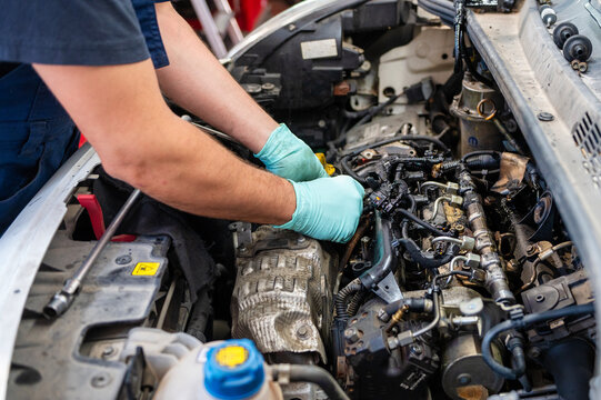 Mechanic repairing a diesel common rail engine with visible oil contamination around the fuel injection system during maintenance in an automotive repair workshop