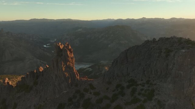 High-angle aerial view of rugged rock formations, mountain ridges, and the river confluence of Valle Encantado, Patagonia, Argentina, illuminated by golden sunset light.