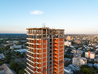 Aerial close-up of high-rise residential building under construction with exposed concrete structure and red brick walls © Exequiel Schuster