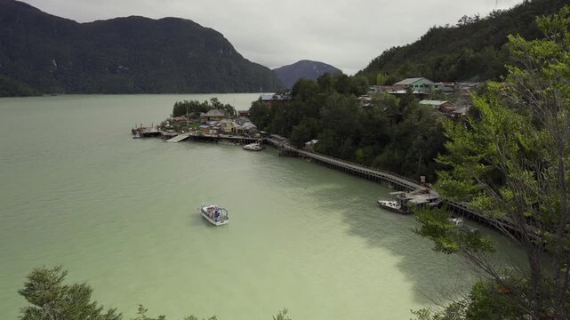 Aerial view of Caleta Tortel, Chile, featuring colorful houses on a forested hillside, wooden boardwalks, and a boat in the bay surrounded by mountains.