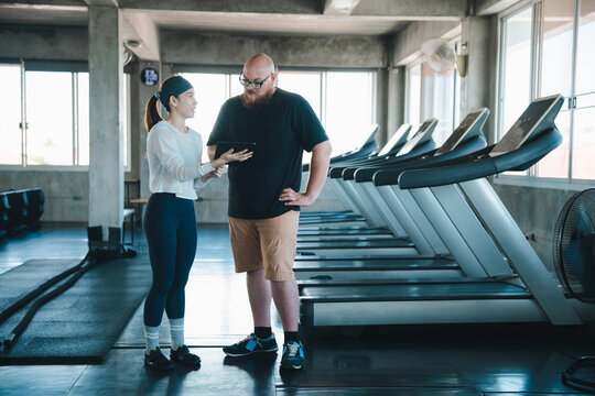 Fitness trainer man gym treadmill coaching tablet exercise workout consultation fitness trainer discussing exercise plan with man using tablet beside treadmill modern gym, coaching workout routine
