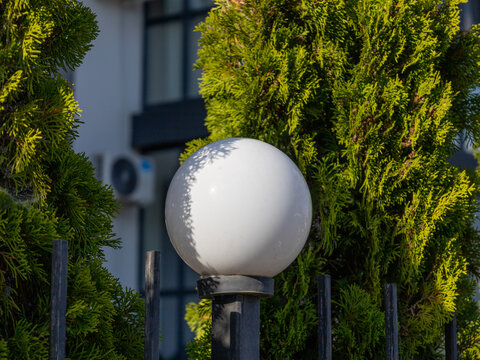 A round light sits on a pole next to green trees outside