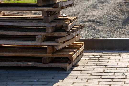 Wooden pallets are arranged in a stack near a brick path