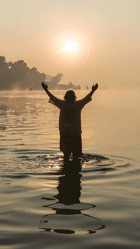 Silhouette mystique d une personne les bras lev&eacute;s pratiquant un rituel spirituel dans un fleuve au lever du soleil