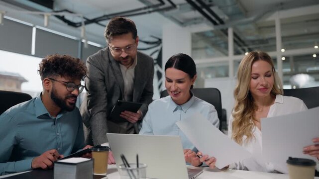 Four multiethnic business managers talking laughing teamwork using laptop reviewing papers documents stats result statistic legal data multiracial businesspeople diversity men women talk work briefing