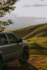 Off-road SUV parked on a scenic mountain hillside during golden hour. Beautiful outdoor landscape with rolling hills. Road trips, overlanding, adventure travel and nature lifestyle themes. © Ivanka
