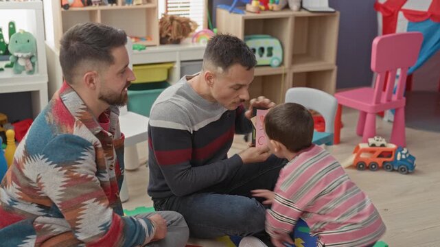 Man showing a banana flashcard to a little boy while sitting on a foam playmat in a building playroom; learning engagement.