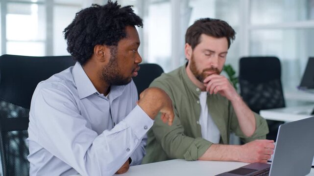 Two diversity business men serious talking looking in laptop African American mentor leader teaching Caucasian worker online work multiethnic businessmen team males talk solving difficulties in office