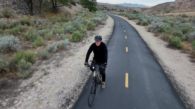Senior man riding an e-bike along a desert nature trail - aerial follow view